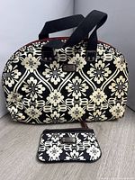 Full view of black and white floral geometric patterned Fossil purse with black handles and matching wallet pouch on gray floor.