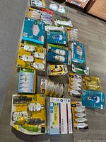 Photo displaying a variety of lightbulbs including spiral CFLs, candle shape incandescents, LED, and multiple packs arranged on a floor.