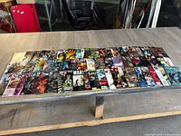 Wide shot of all 60 comic books spread in rows on a wooden table showing various titles and colorful covers.