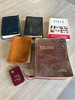 Lot of six Bibles, various sizes and bindings, arranged on light wood floor
