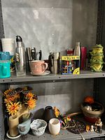 Top shelf with water bottles, mugs, boxed mug set, and decorative ceramic frog figurines