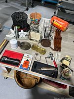 Photo showing a variety of household and kitchen items arranged on a table including baskets, paper towel holders, brass trays, and a sleeping pad.