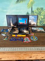 Wide view of table featuring framed rocket launch photos and various NASA patches and decals laid out in front.