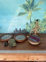 Photo of two camouflage-themed clocks, pair of small black binoculars with camouflage pouch, and two metal canteens on wooden surface