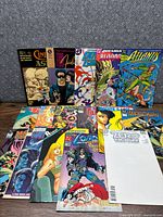 Front view of the 16 comics arranged upright in two rows on a carpeted floor showing colorful covers and various titles