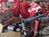 Red crate with various old Coca-Cola and other soda bottles, Coca-Cola towel, and two Coca-Cola notebooks visible, bottles are empty and for display only.