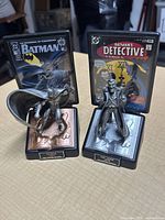 Photo showing the full lot of two pewter figurines, Batman and Joker, each with their comic cover backgrounds and bases with name plates.
