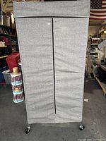 Front view of the grey fabric-covered rolling wardrobe with front zipper and caster wheels.