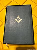 Front cover of the Bible with gold Masonic symbol on dark green leather.