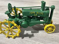 Photo of green vintage cast iron John Deere tractor toy showing side profile with yellow spiked wheels and embossed 'John Deere D' text.