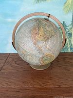 Full view of vintage Replogle globe on wooden surface with tropical wallpaper background showing 3-D terrain and metal stand.