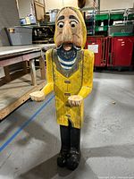 Full frontal view showing figure's yellow raincoat, blue and white striped shirt, black boots, and outstretched hands.