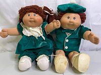 Front view of two Cabbage Patch Kids twin dolls seated side by side, showing full outfits and bodies.