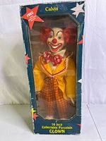 Full front view of the clown doll in original box, showing red curly hair, painted face and colorful outfit.