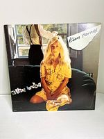 Front cover of Kim Carnes Mistaken Identity vinyl record album showing Kim Carnes seated in yellow dress on a couch with a man standing behind her.