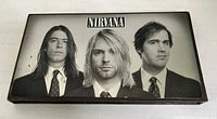 Front view of metal box cover featuring black and white image of Nirvana band members Kurt Cobain, Dave Grohl, and Krist Novoselic in suits.
