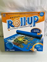 Front view of the retail box showing Puzzle Roll-Up mat with image of mat holding puzzle pieces and text indicating compatibility with up to 1500 pieces.