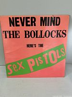 Front cover of the vinyl album with orange background and bold black and green text saying 'Never Mind the Bollocks Here's the Sex Pistols'.