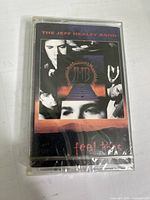 Front view of cassette tape in jewel case with cover art showing album title and band images