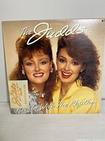 Front cover of The Judds 1985 vinyl record "Rockin With The Rhythm" showing the two artists with styled hair, album title, and tour sticker.