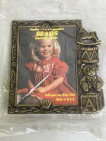Front view of brass photo frame featuring vintage Sears Portrait Studio branding and stacked baby toys design.