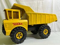 Side view showing yellow metal dump body, cab with clear windows, black exhaust pipes, and large black rubber tires with Tonka and XMB-975 branding.