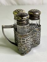 Silver-plated carrier holding three glass shakers with silver-plated tops showing signs of tarnish and wear.
