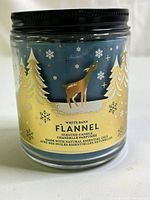 Front view of white barn flannel scented candle showing label with deer, pine trees, and snowflakes