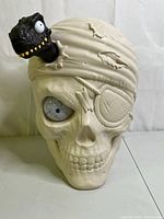 Front view of off-white skull container showing closed eye and attached dinosaur figure.