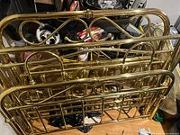Photo showing multiple brass bed frames stacked, revealing headboards and footboards with looping decorative brass designs.