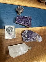 Wide shot showing six ametyst and crystal pieces on a wood and blue surface including a large amethyst slab and clear quartz point.