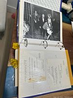 Binder open to a page showing a black and white photo of men in formal attire and typed documents with visible text.