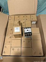 Open cardboard box containing 25 individual brown boxes and one contactor resting on top.
