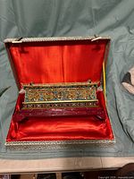 Open hinged case showing red satin interior and cloisonné piece inside