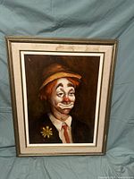 Full view of signed clown painting on panel in gold-toned frame against fabric backdrop