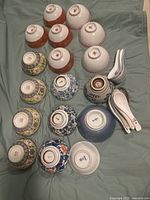 Photo showing the variety of porcelain bowls turned upside down to reveal different maker's marks, stamps, and designs, many with traditional Asian motifs and patterns, as well as 7 stacked white serving spoons with blue decoration.