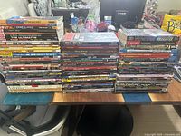 Full overview photo showing large stacks of graphic novels and comic books on a table, showcasing the size and variety of the lot.