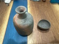 Top angle view of the pottery bottle and small dish on a wood table with blue runner.