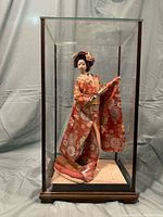 Front view of porcelain doll in floral kimono inside glass display case.
