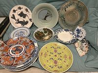 Overall view of 14 plates arranged showing their variety in styles and colors including blue and white, yellow and multicolor, and abstract earth tones
