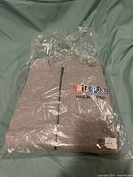 Folded gray hoodie in plastic wrapping with visible Hairspray The Musical logo embroidered on chest.