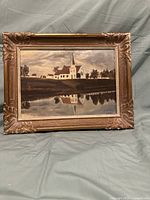 Frontal view of oil painting on board showing church and water reflection in ornate gold frame.