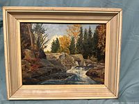 Front view of the oil painting in its frame showing a natural waterfall scene with autumnal trees and rocks.