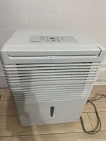 Full front view of white plastic Premiere dehumidifier showing vent grill and water level indicator window near base.