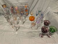 Full group of 18 crystal champagne flutes and additional colored stemware on white cloth background.