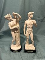 Front view of two sculptures replicas. Left: female figure leaning on a pillar. Right: male nude resembling Michelangelo's David.