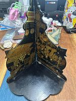 Photo showing the corner wall shelf from above highlighting the black lacquer and intricate gilt Japanese imagery on the vertical panels and flat base.
