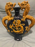 Front view of a dark blue pottery vase with two yellow-orange dragon handles and central dragon design