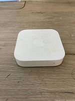 White Apple AirPort Express Base Station on wooden surface showing top with Apple logo and visible dirt spots.