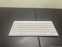 Front and angled side view of Apple wireless Bluetooth keyboard, showing full keyboard layout and white keys with aluminum back plate.